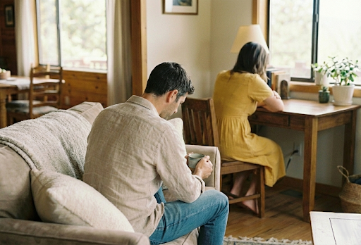 Man on a sofa using his phone while his partner sits apart by the window